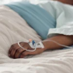 Healthcare, hand and iv with a patient in a hospital bed for recovery or rehabilitation closeup. Medical, wellness and treatment with a sick person lying in a clinic on a saline solution drip