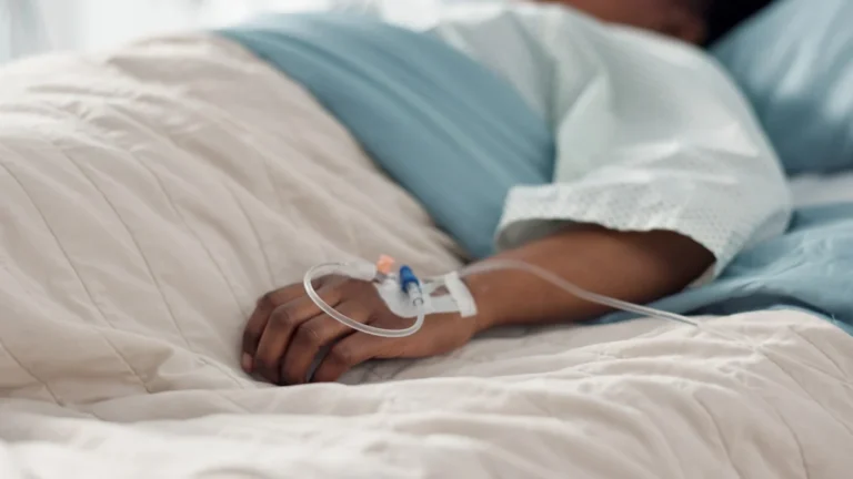 Healthcare, hand and iv with a patient in a hospital bed for recovery or rehabilitation closeup. Medical, wellness and treatment with a sick person lying in a clinic on a saline solution drip