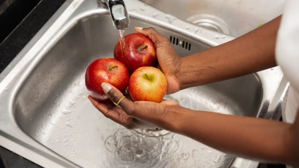 close up of Hands Rinsing Red Apples Under Tap Water in a Stainless Steel Kitchen Sink