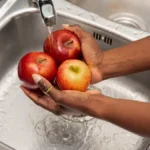 close up of Hands Rinsing Red Apples Under Tap Water in a Stainless Steel Kitchen Sink