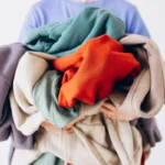 Person holding large pile of colorful clothes close-up on white background