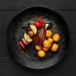 Top view of grilled beef with vegetables and potato balls on a plate