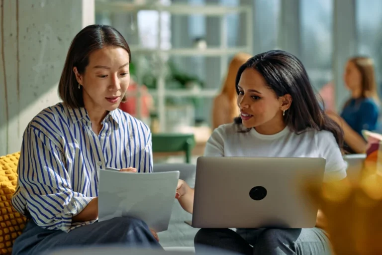 Businesswomen collaborating on project, discussing documents and laptop